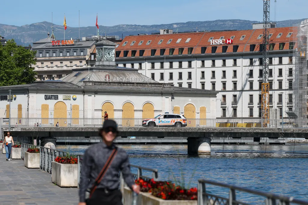 A police car patrols a bridge over a river in Geneva, in front of boarded-up buildings and the HSBC bank building.