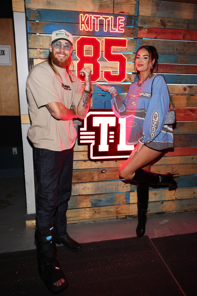 George and Claire Kittle posing in front of a red neon sign that reads 