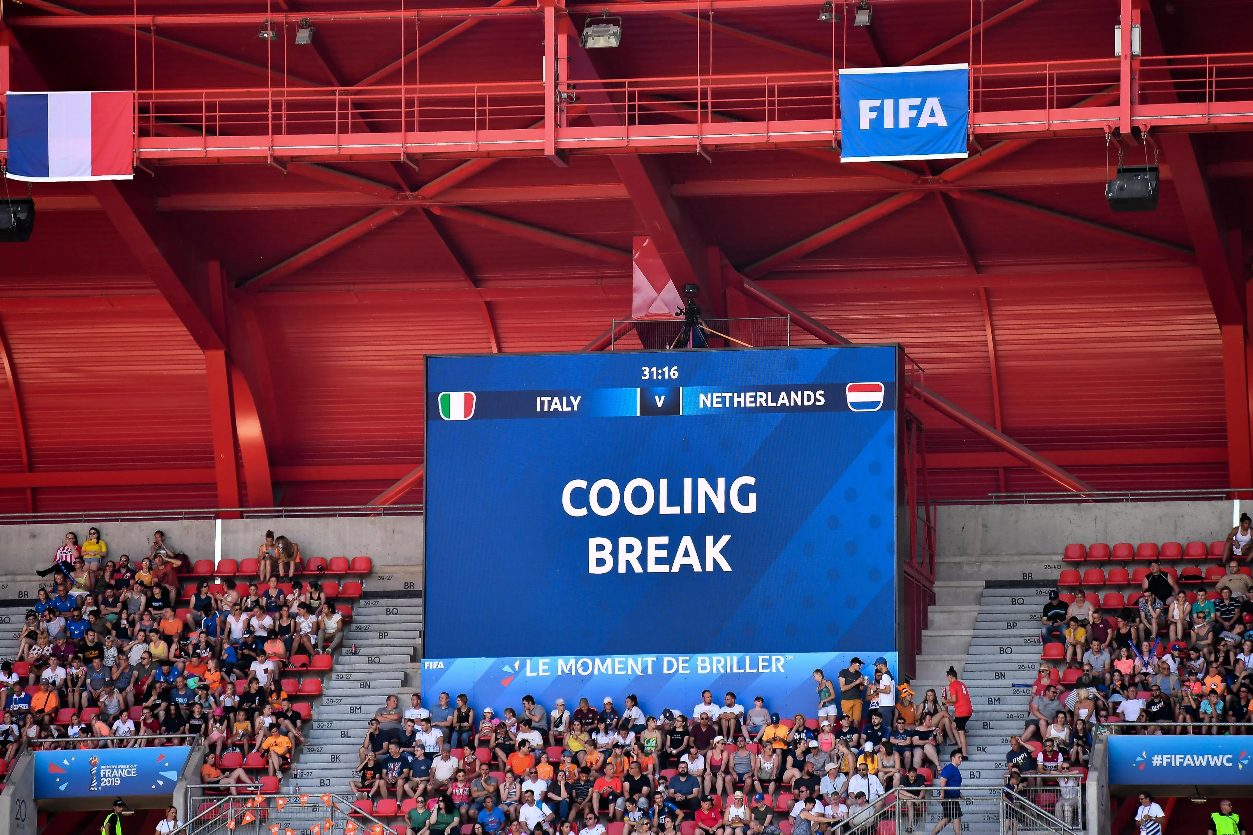 a sign in a soccer stadium displays the message: “cooling break” with fans seated below 