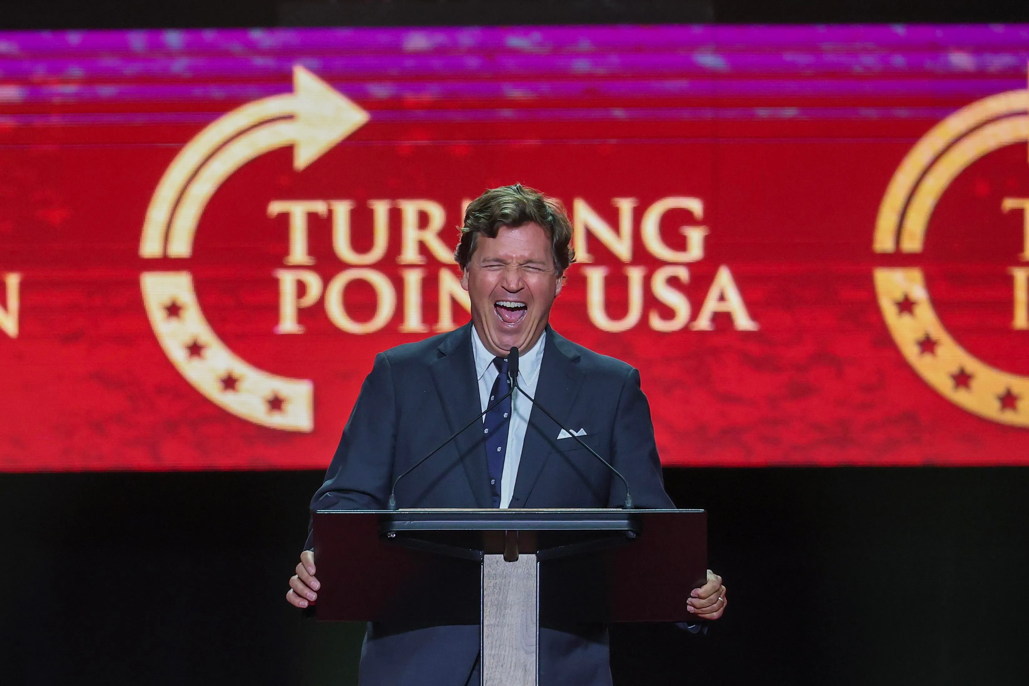Tucker Carlson at a podium for a TPUSA event