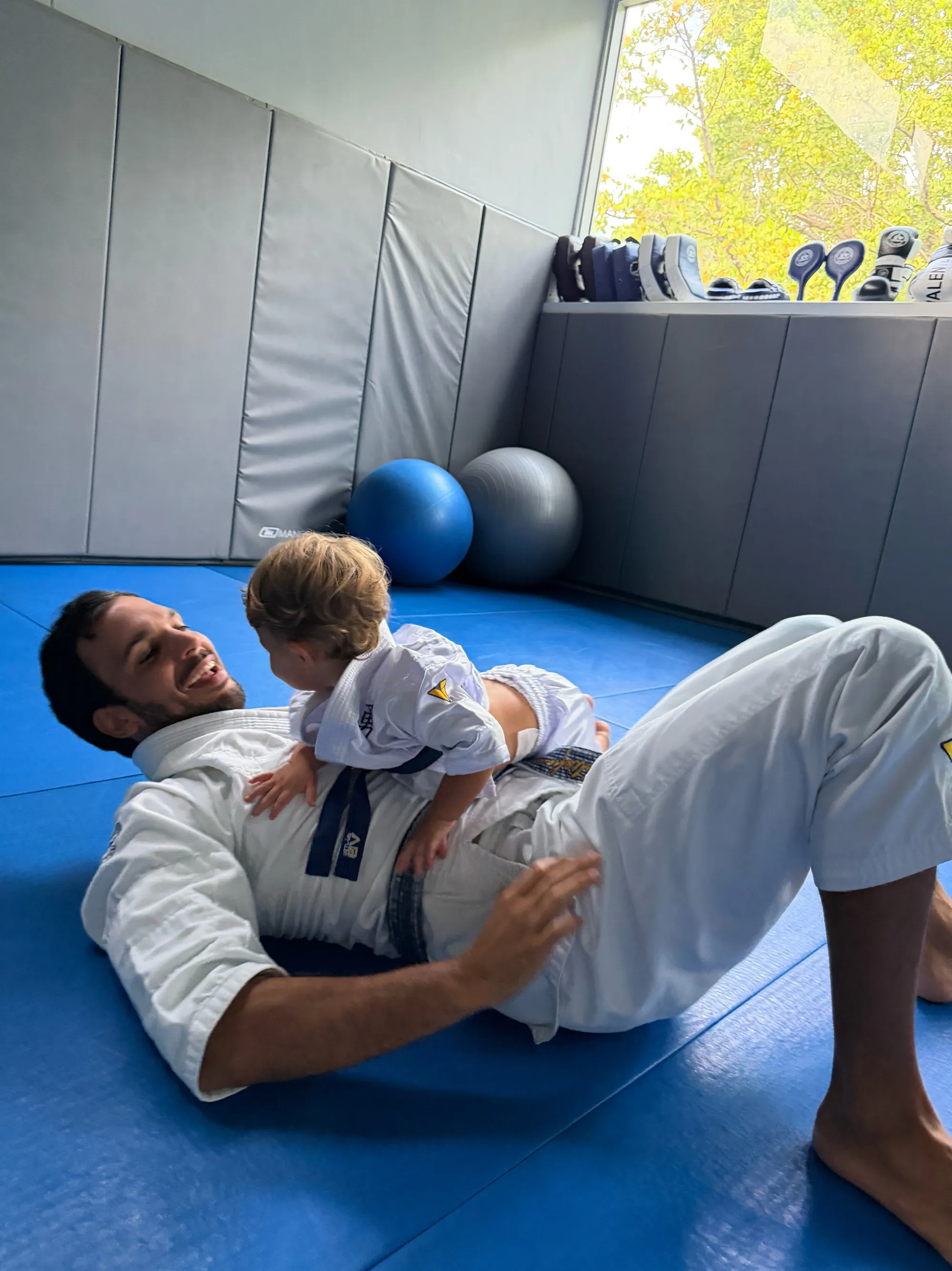 Joaquim Valente and child in martial arts uniforms on a blue mat.