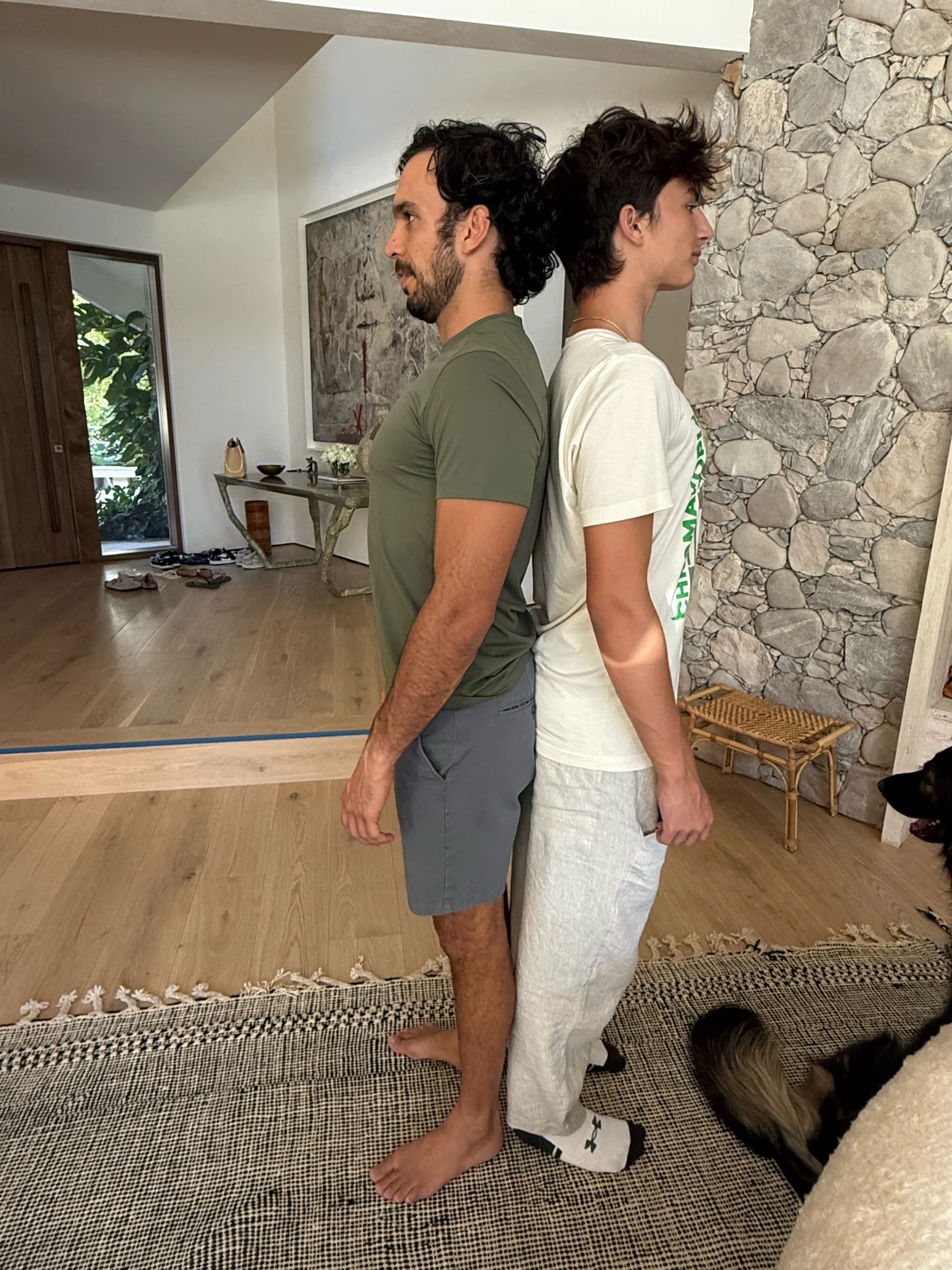 Joaquim Valente and another man standing back to back, with a dog lying on a rug beside them.