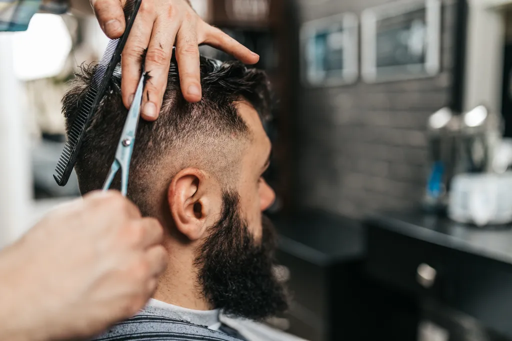 A barber cutting a man's hair with scissors and a comb.