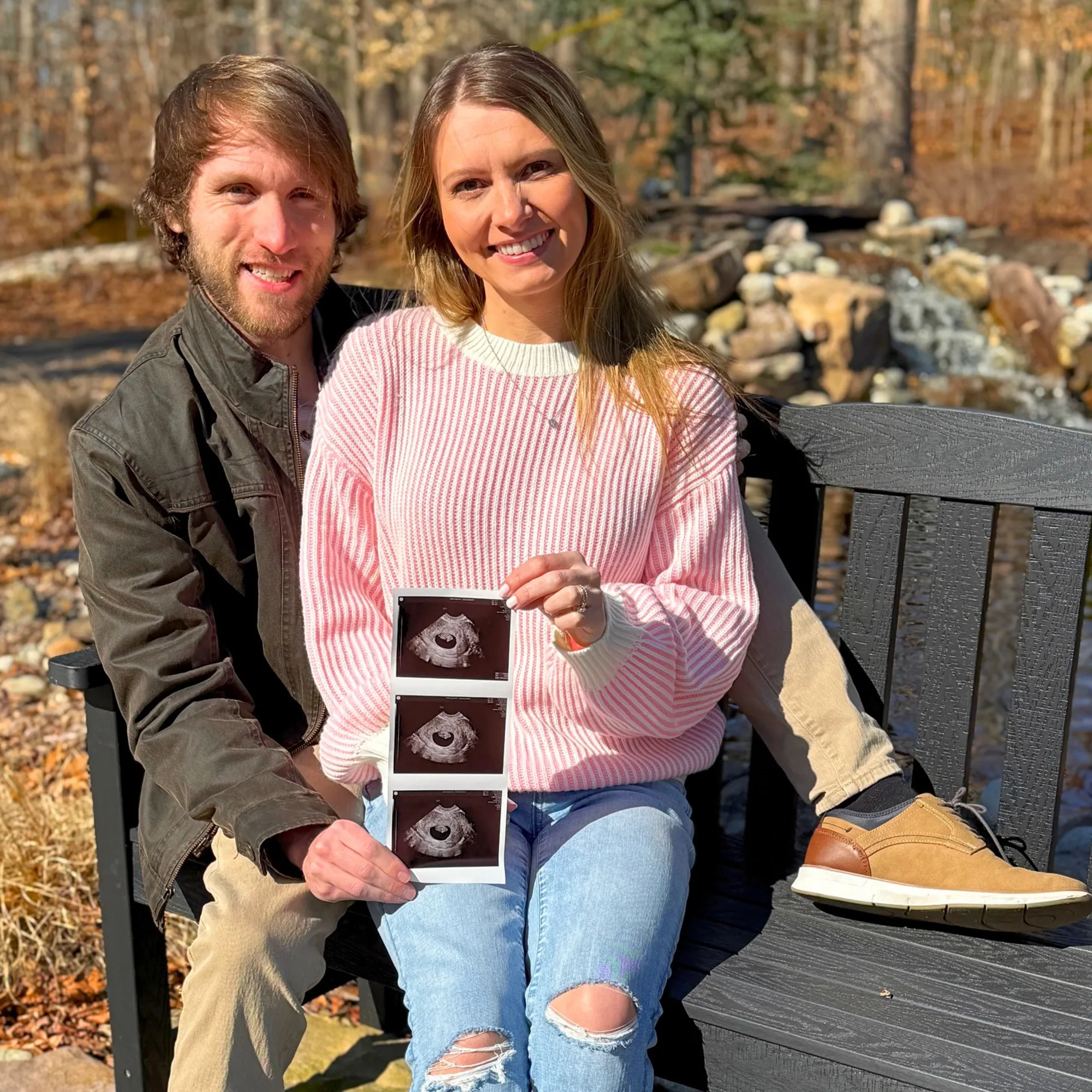 YouTuber Jesse Ridgway and his wife, wearing a pink sweater and ripped jeans, smiling and holding ultrasound photos.