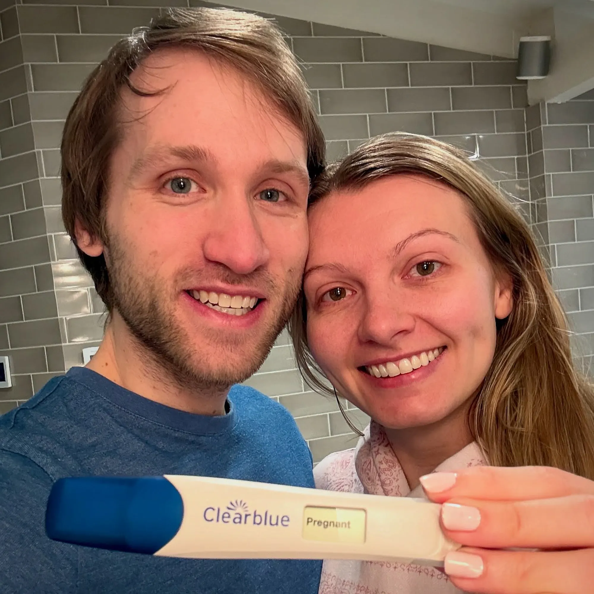 Jesse Ridgway and his wife smile while holding a Clearblue pregnancy test with the word 