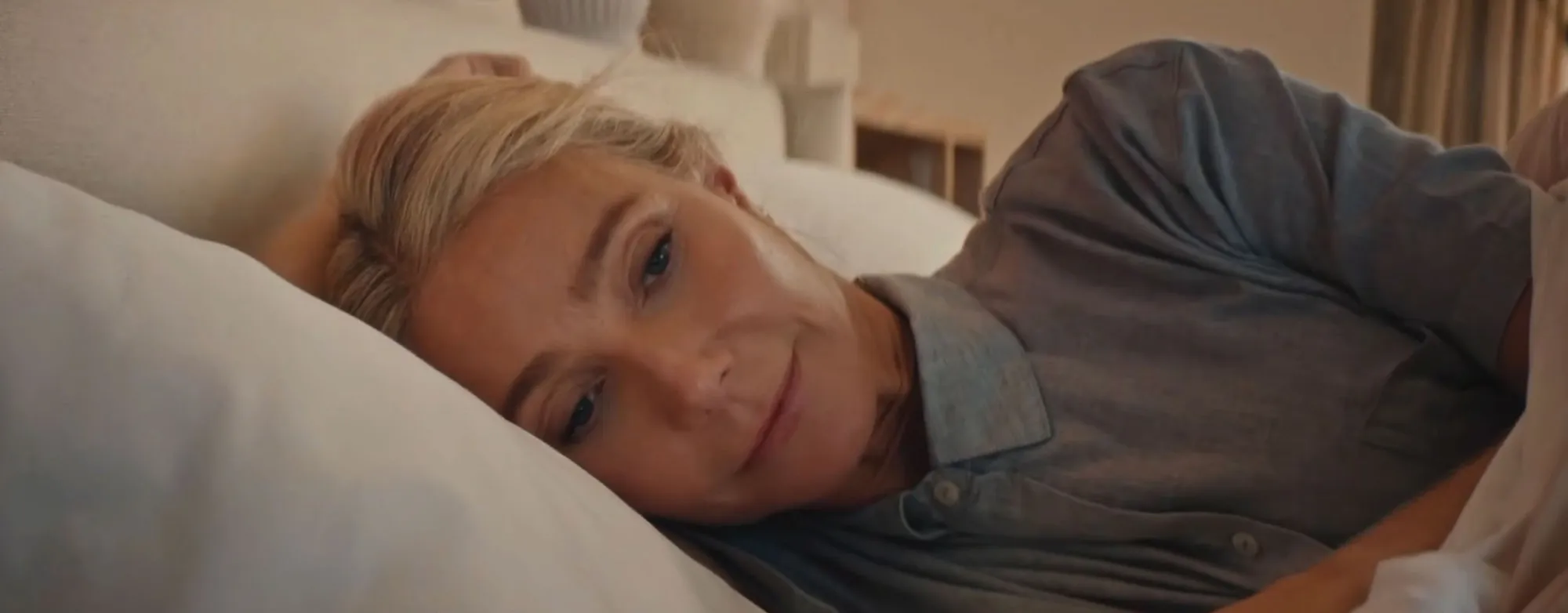 Gwyneth Paltrow lying in bed, wearing a grey shirt.