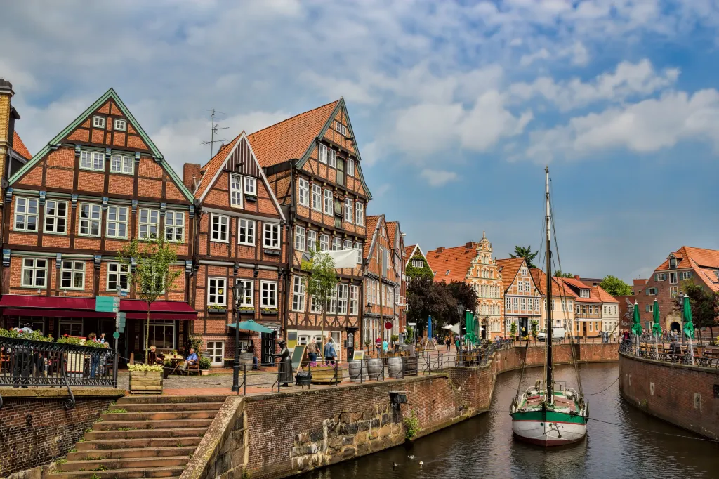 The historic harbor of Stade, Germany, featuring a canal with a moored sailboat, lined by traditional brick and half-timbered houses with outdoor cafes.