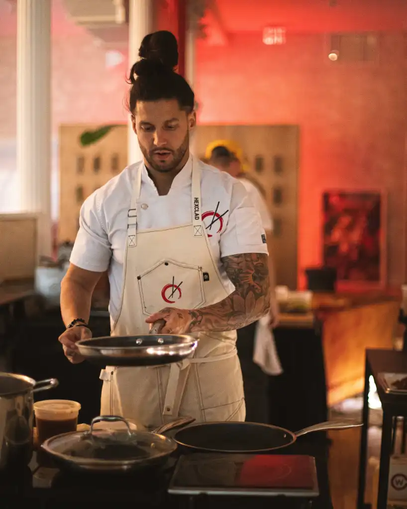 Robbie Felice, co-founder and chef-partner of pastaRAMEN, cooking on a stove with a red glow in the background.