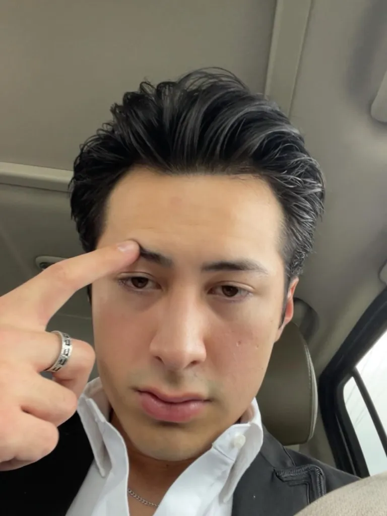Hudson Williams with his finger touching his eyebrow.