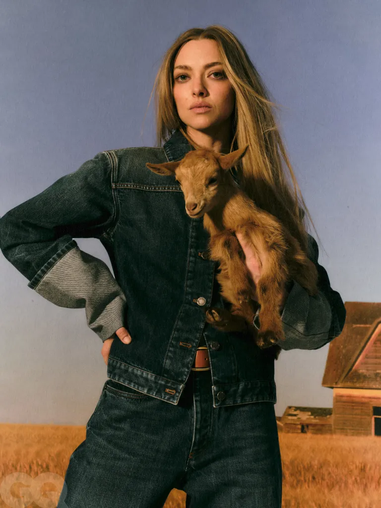Amanda Seyfried wearing a denim jacket and jeans, holding a baby goat.
