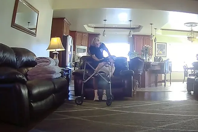 A woman using a walker in a living room, with a kitchen visible in the background.