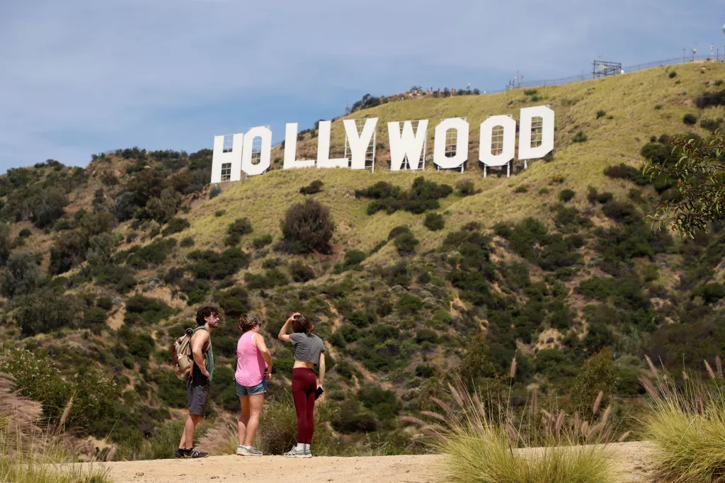 Three hikers on a trail with the Hollywood sign on a grassy hill in the background.