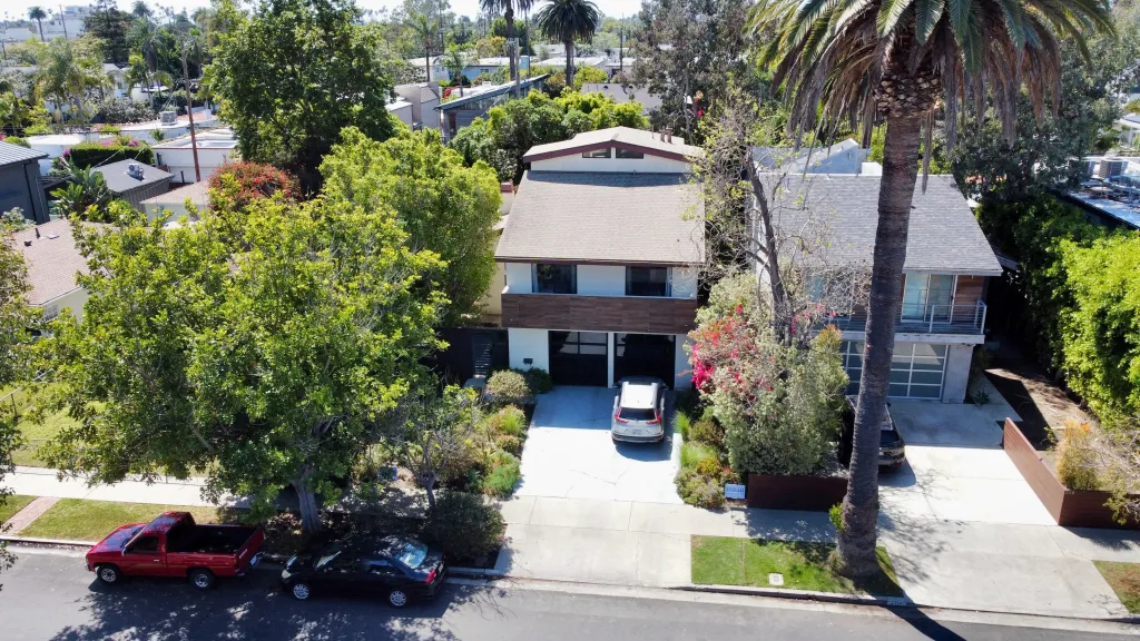 Aerial view of Faizah Malik's home at 2125 Glyndon Ave, Venice, CA 90291, featuring a house with a garage and a car parked in the driveway, surrounded by lush trees and landscaping.