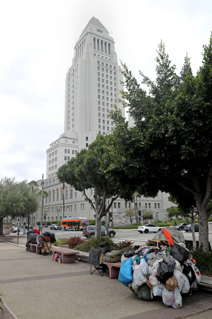 Homeless encampment and belongings piled on a bench in front of Los Angeles City Hall.