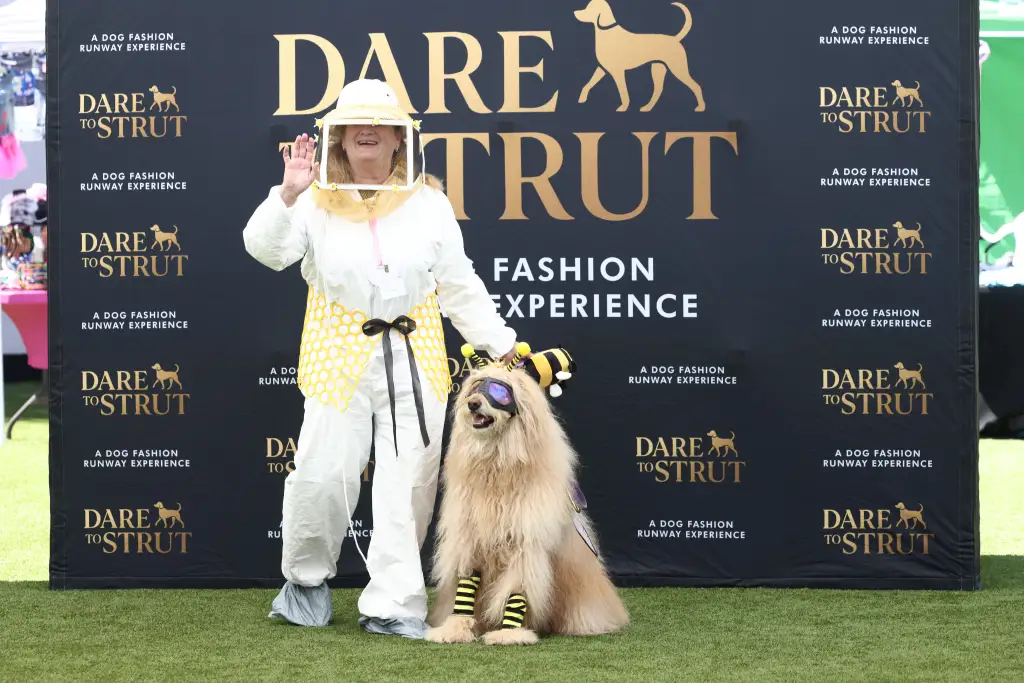 Gail in a beekeeper suit with Honey the therapy dog in a bumblebee costume at the 