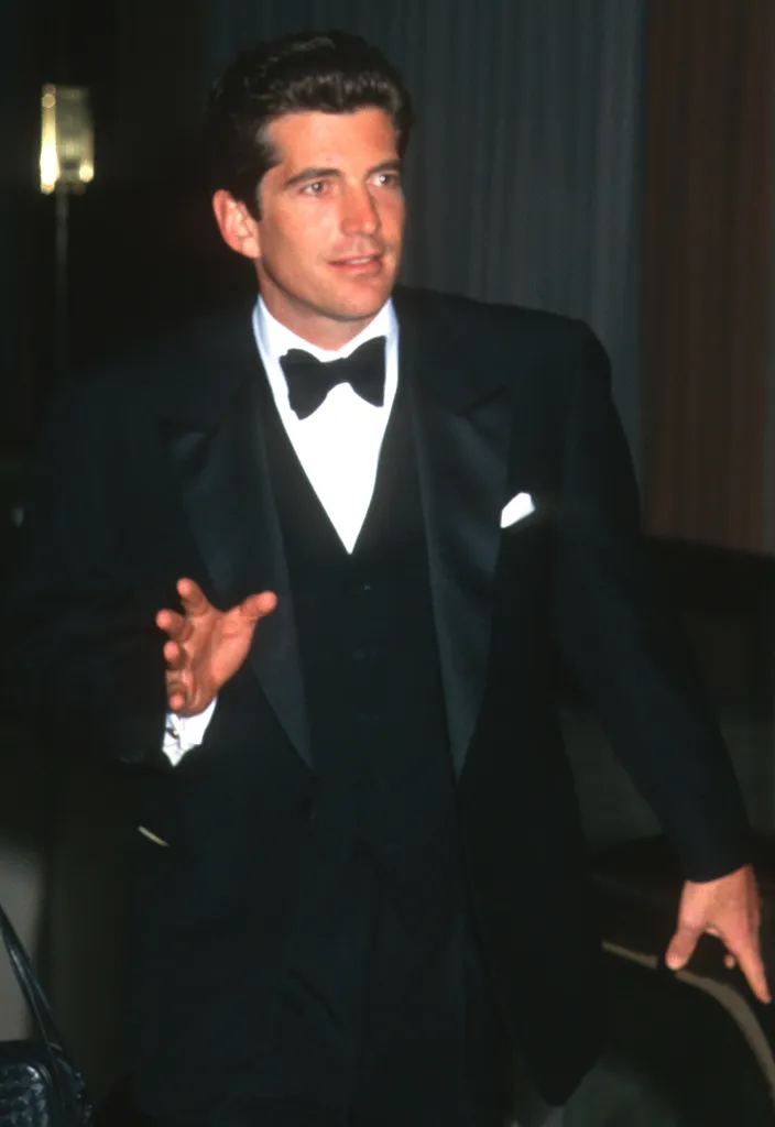 John F. Kennedy Jr. in a black tuxedo with a black bow tie and white pocket square.