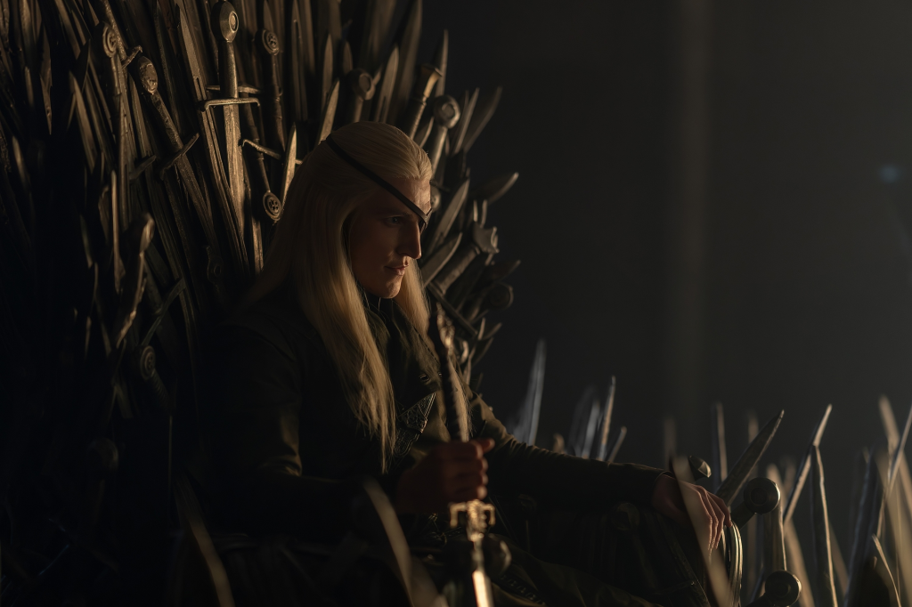 Aemond Targaryen, wearing an eyepatch, seated on the Iron Throne.