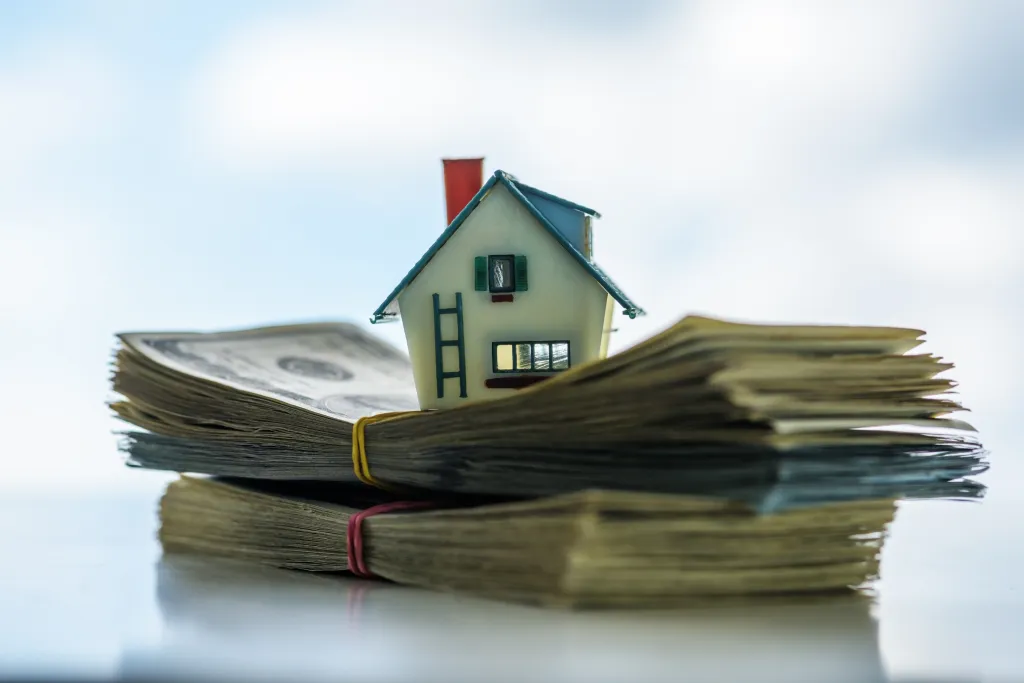 A miniature model house sitting on stacks of cash.