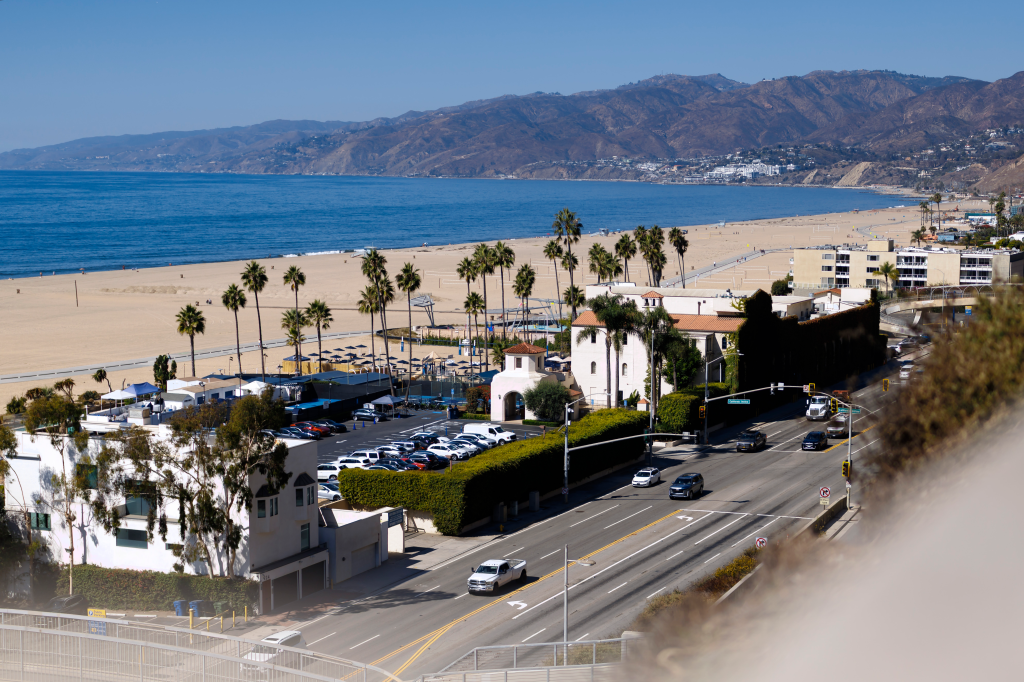 Aerial view of Santa Monica Beach, California, with beachside buildings, a highway, and mountains in the background.