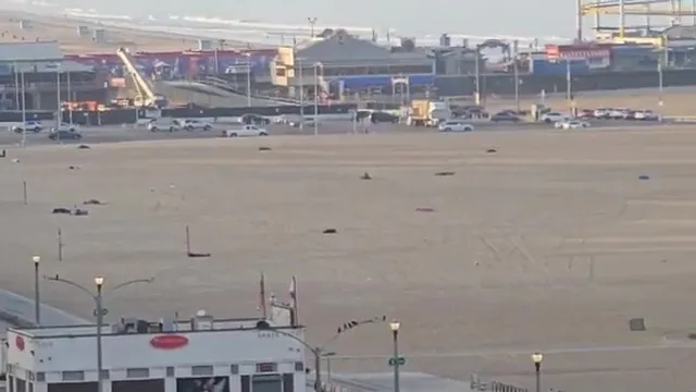 Santa Monica beach at sunrise, with numerous dark shapes, possibly sleeping bags, scattered across the sand.