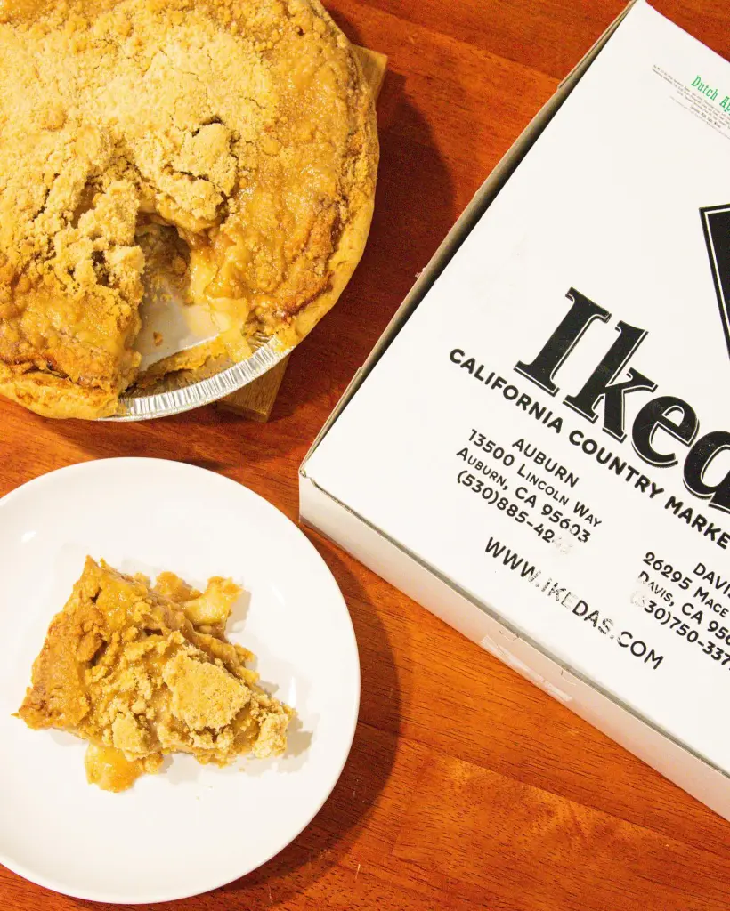 An apple pie with a slice missing, next to a white box from Ikeda's California Country Market.