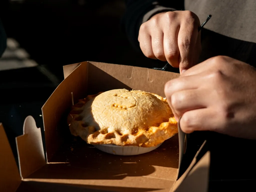 Person eating a small pie from a cardboard box.