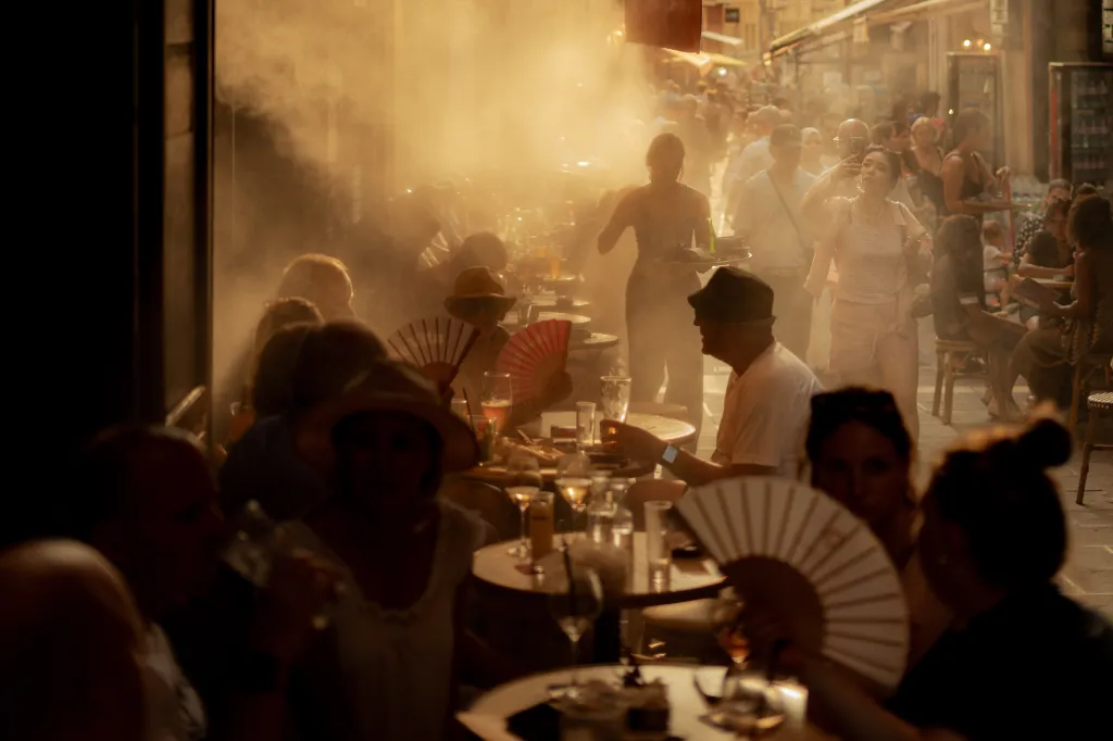 Customers seated at outdoor cafe tables and pedestrians walk through mist from a cooling system on a street in Nice, France.