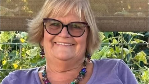 A smiling woman with blonde hair, glasses, and colorful jewelry.