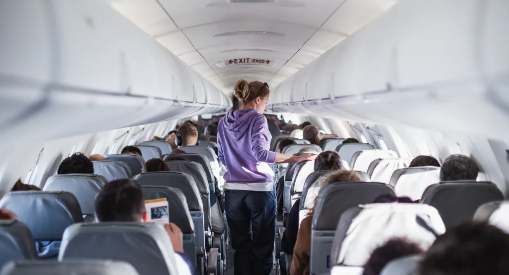 A female traveler walks down the aisle of an airplane filled with passengers.