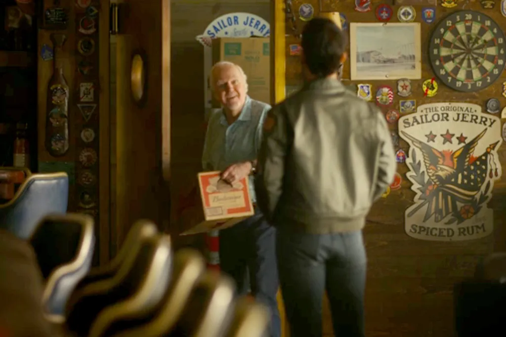 James Handy as bartender Jimmy in Top Gun Maverick, holding a box of Budweiser.
