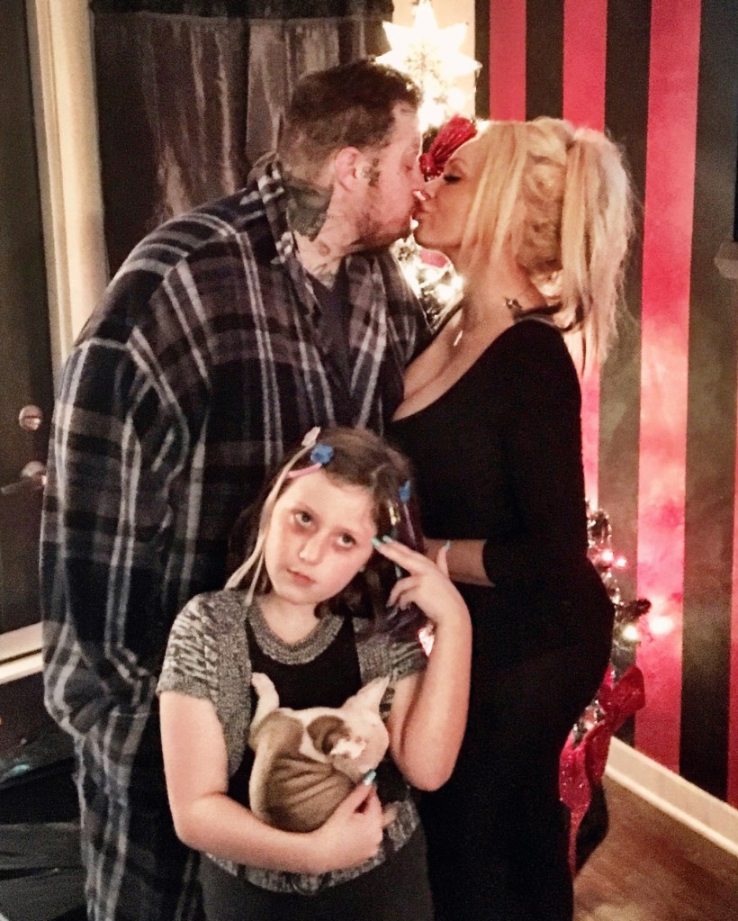 Jelly Roll and Bunnie Xo kiss while a young girl holding a puppy looks at the camera.