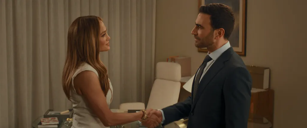 Jennifer Lopez and Brett Goldstein shake hands in an office scene.