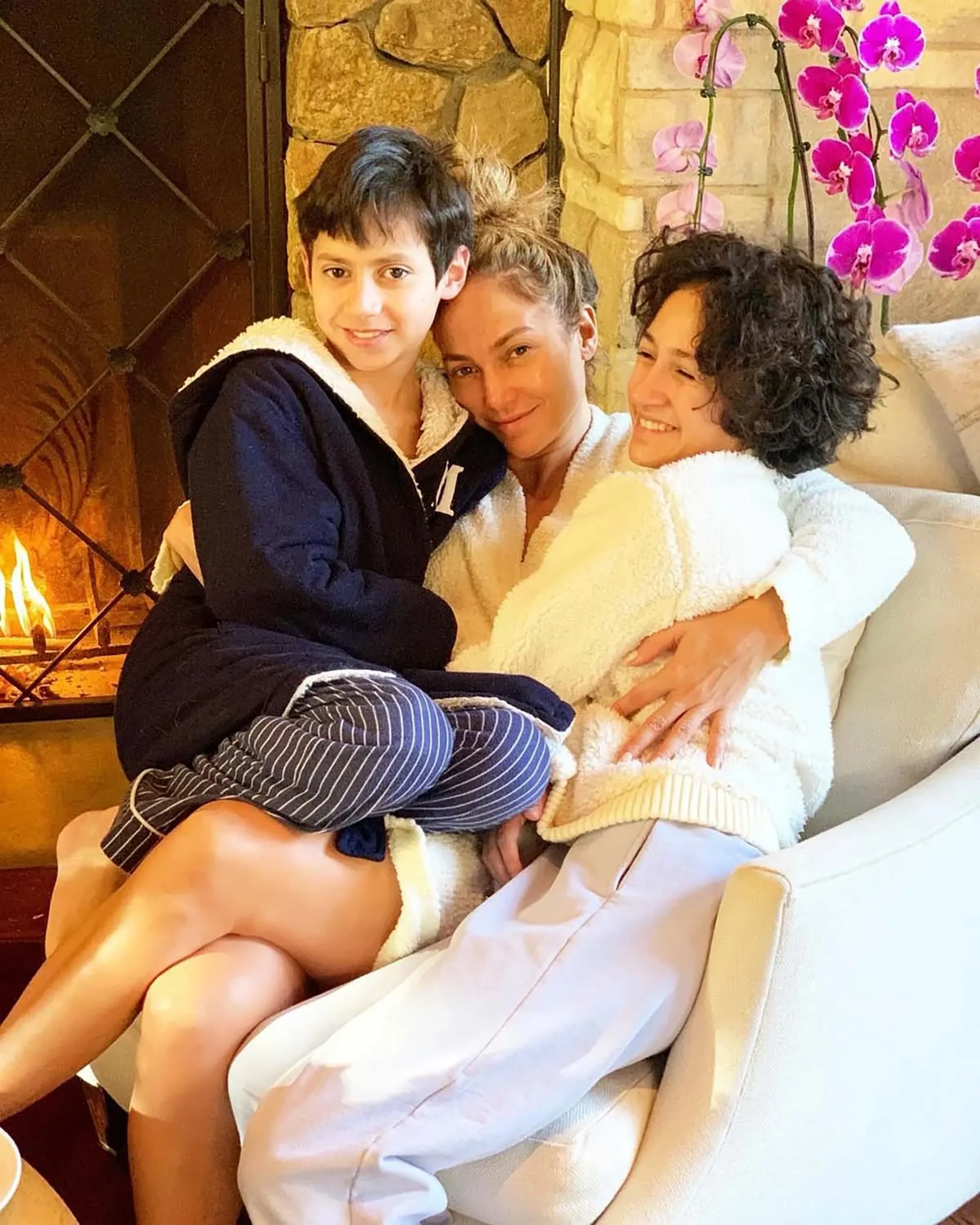 Jennifer Lopez hugging her twins, Emme and Max, in front of a fireplace.