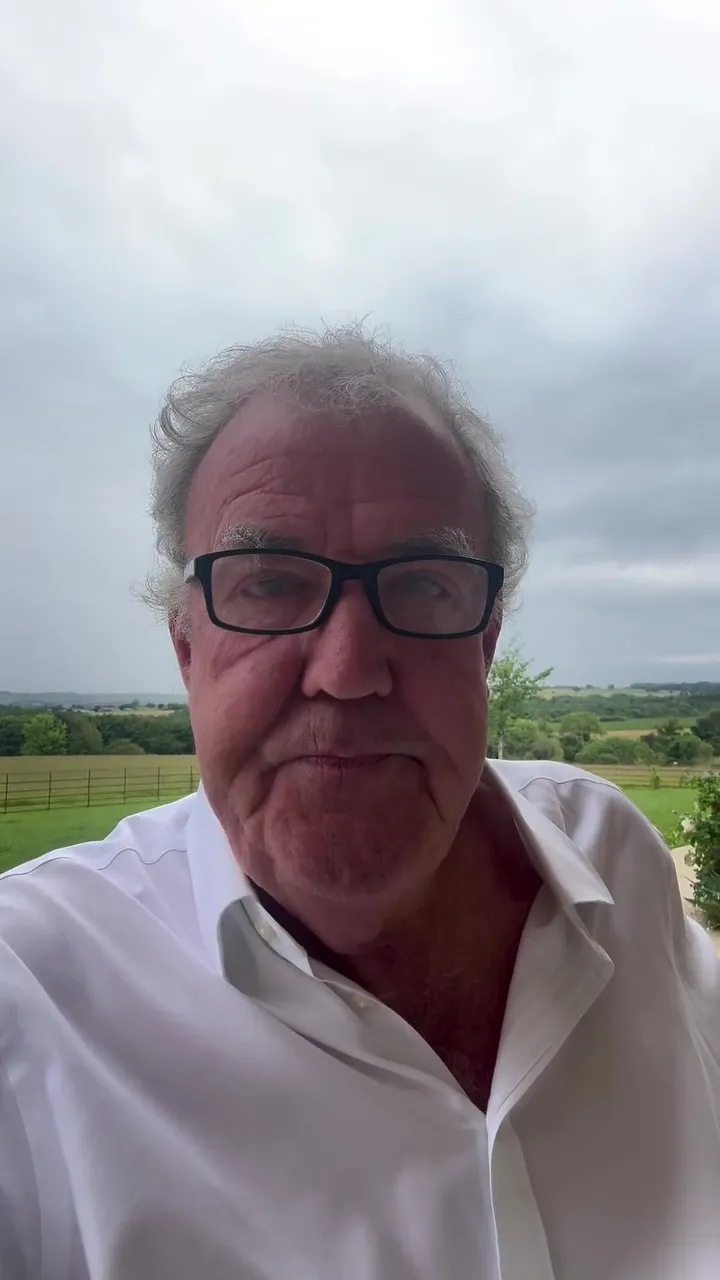 Jeremy Clarkson in a white shirt and glasses, with a blurred field and sky in the background.