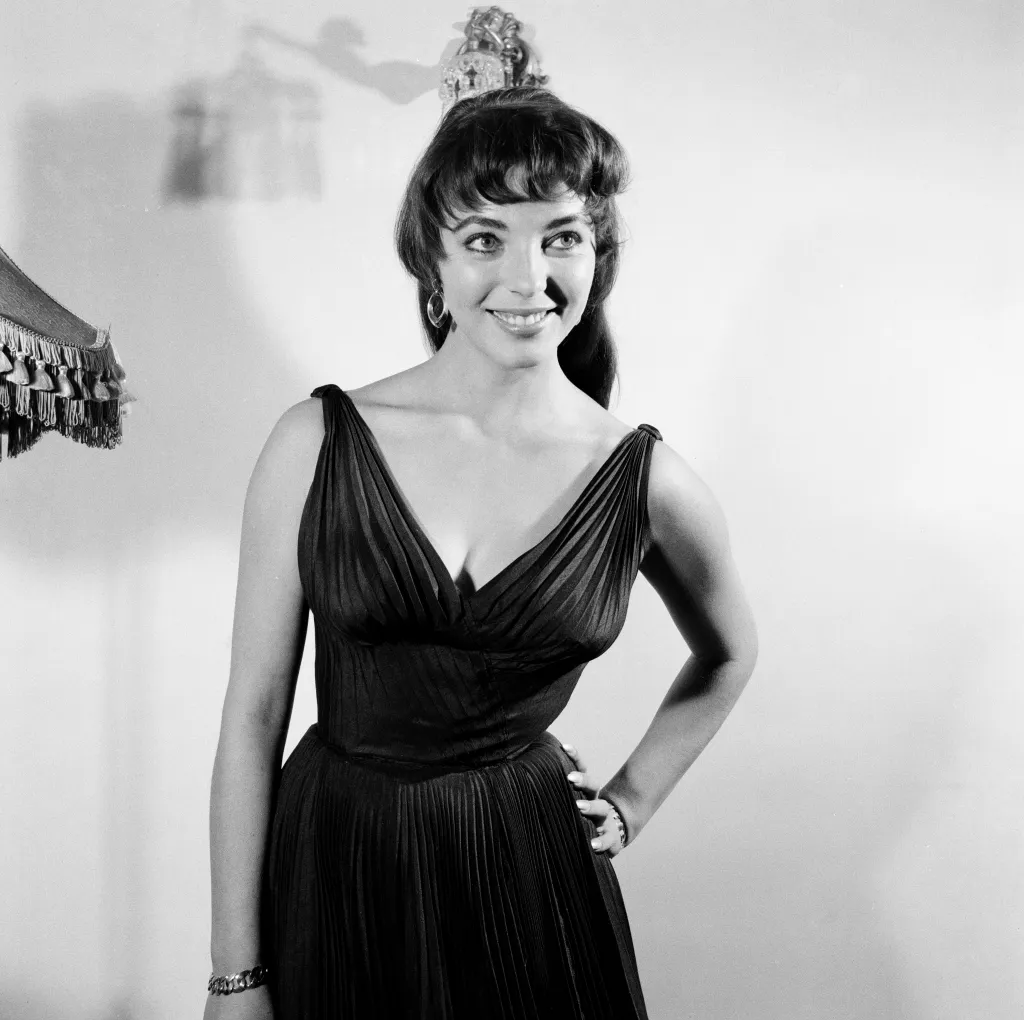Joan Collins at 22, posing in a black silk cocktail dress.