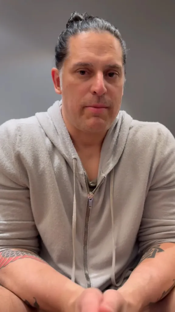 Joe Manganiello wearing a gray hooded sweatshirt, looking directly at the camera.
