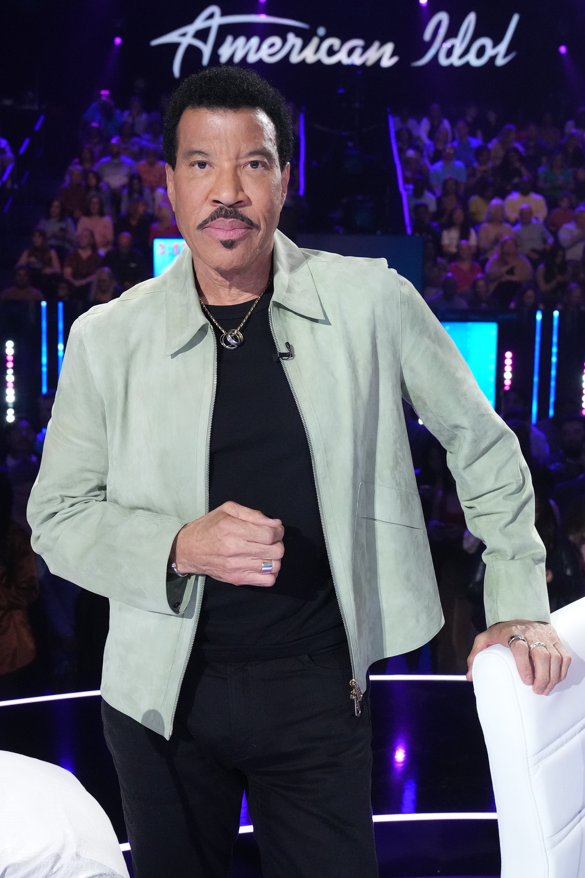 Lionel Richie, an American Idol judge, stands facing forward on the set of the show.