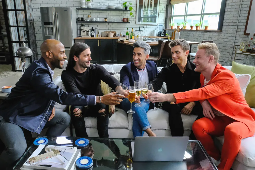 The Queer Eye cast members Karamo Brown, Jonathan Van Ness, Tan France, Antoni Porowski, and Bobby Berk toasting with champagne glasses.