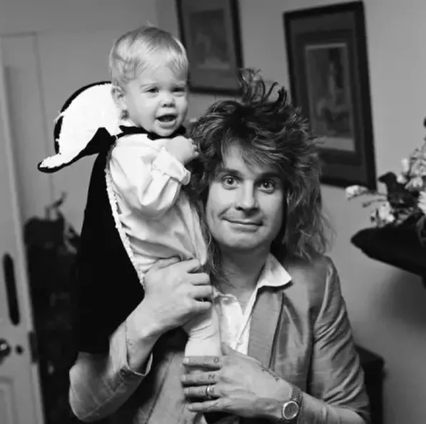 Ozzy Osbourne holding a child in a costume on his shoulders.