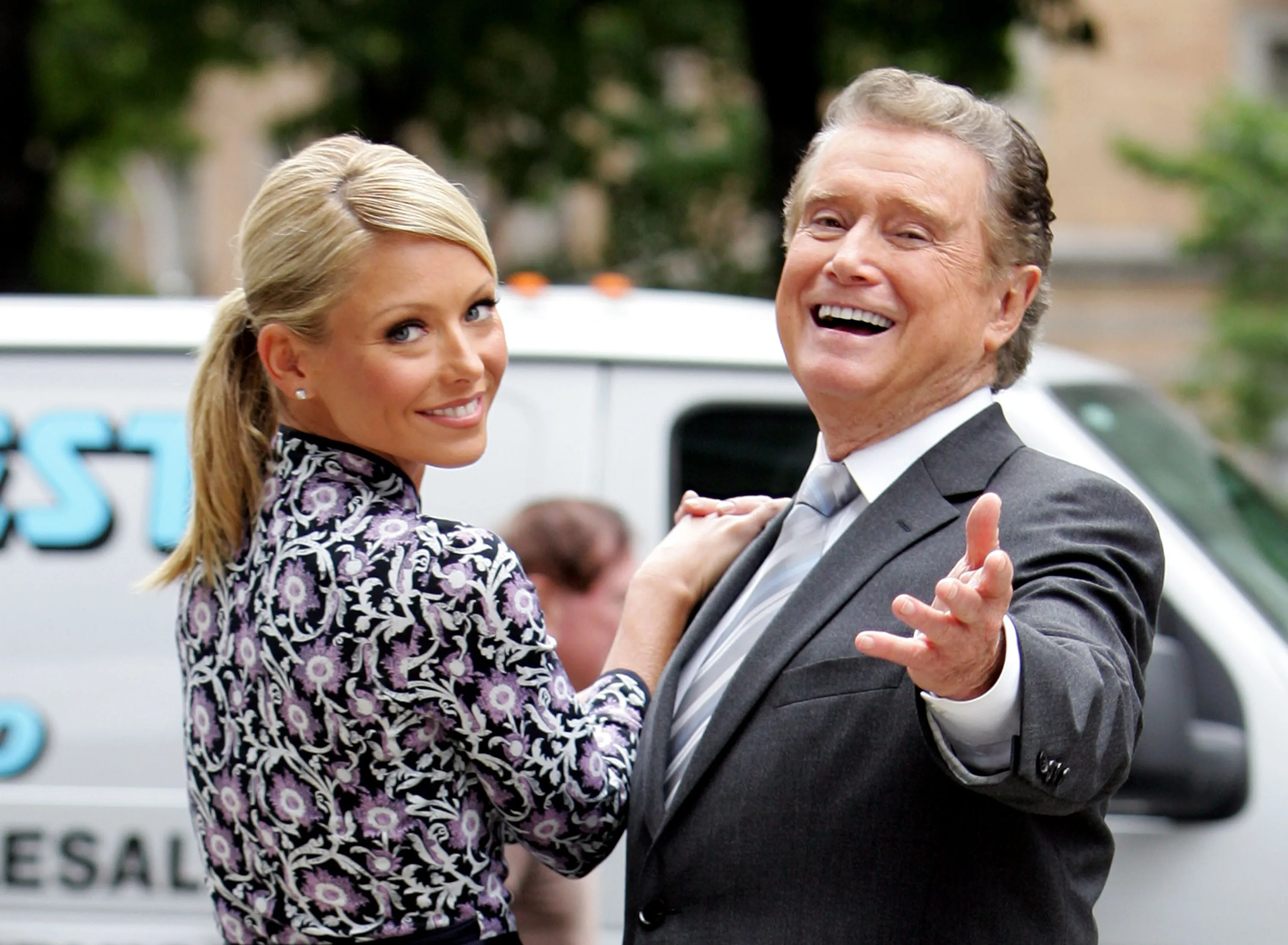 Kelly Ripa and Regis Philbin smiling and filming a commercial.