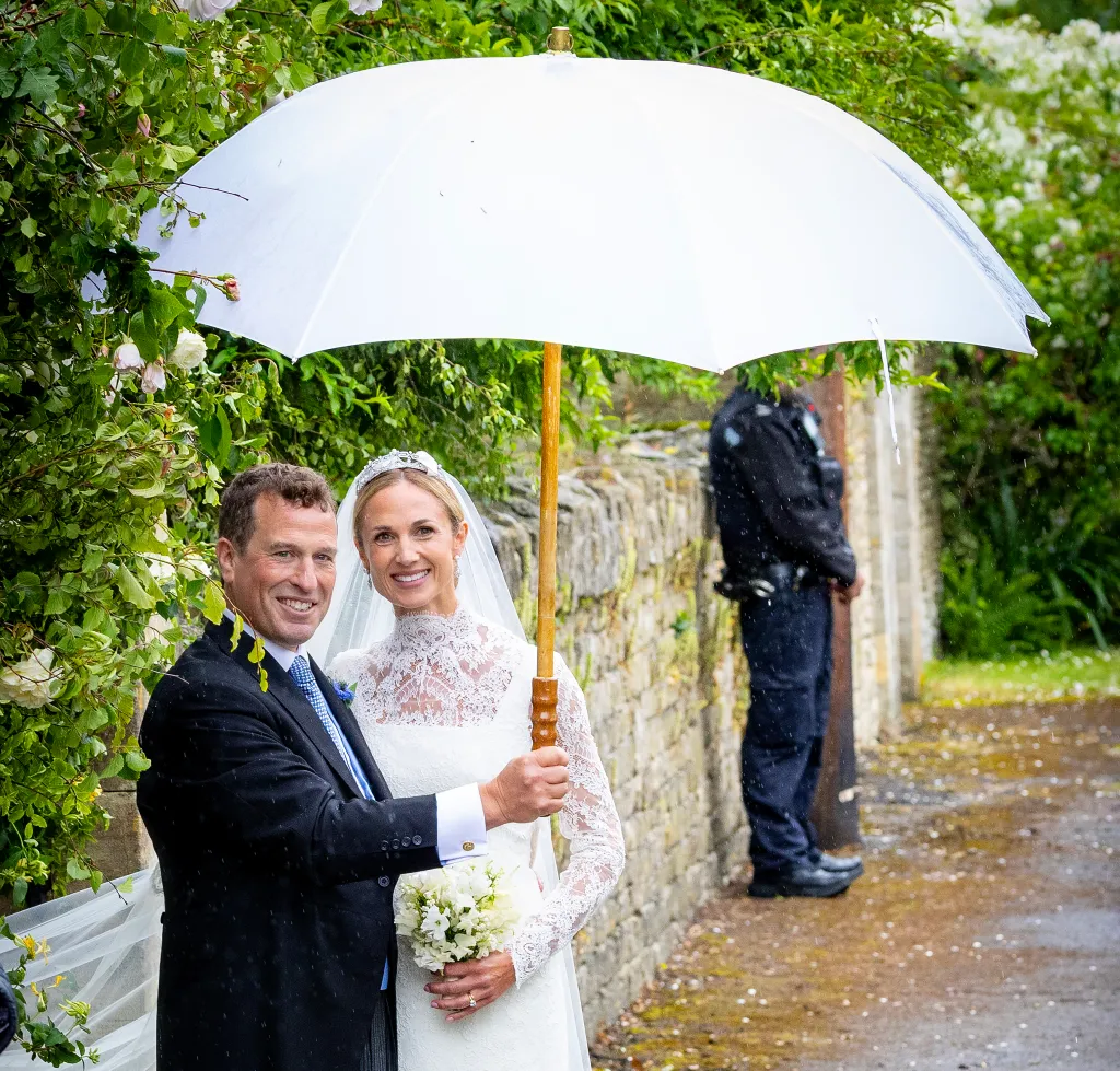 Peter Phillips and Harriet Sperling smiling under an umbrella after their wedding ceremony.
