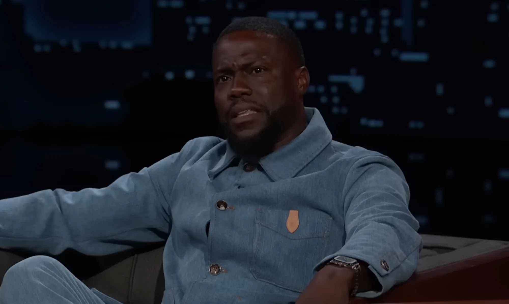 Kevin Hart in a blue denim jacket on a talk show.