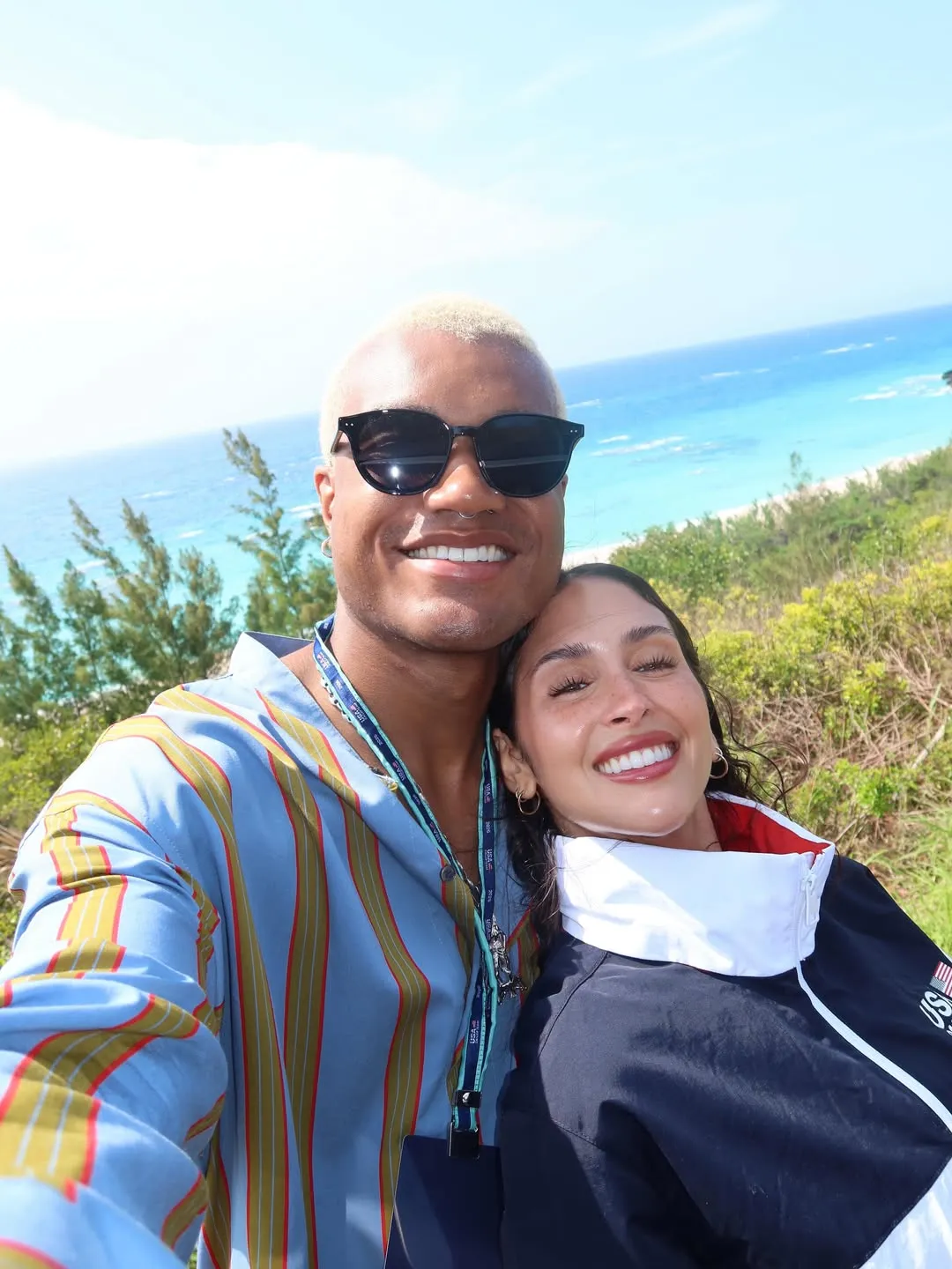 Musician KJ Dillard and Dara Levitan smiling for a selfie with an ocean view behind them.