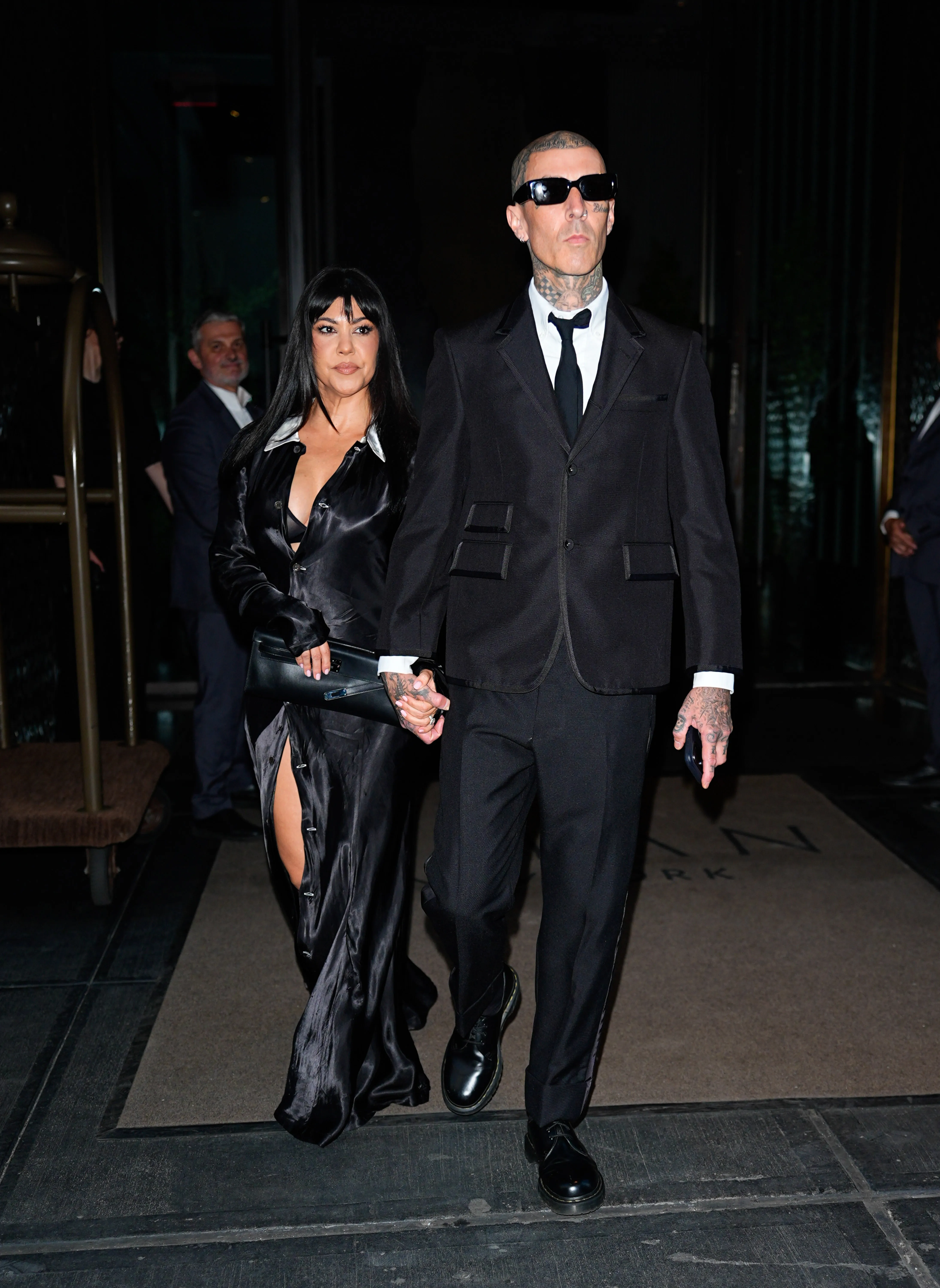 Kourtney Kardashian and Travis Barker hold hands while walking outdoors.
