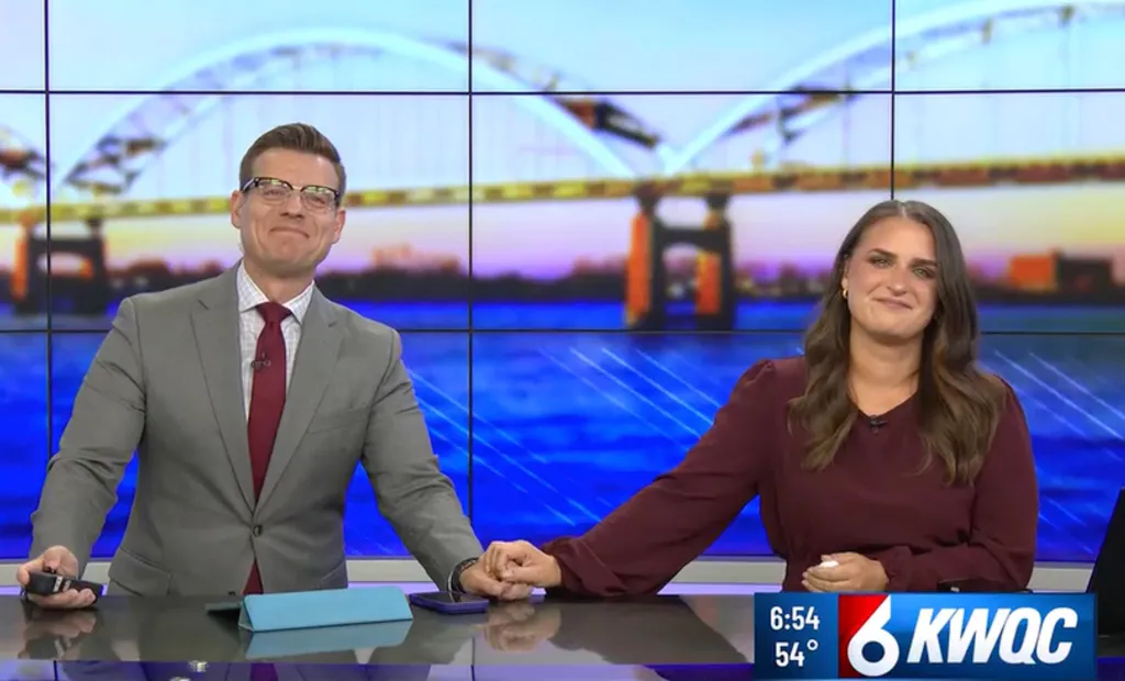 Morning anchors Dustin Nolan and a female colleague holding hands at a news desk.