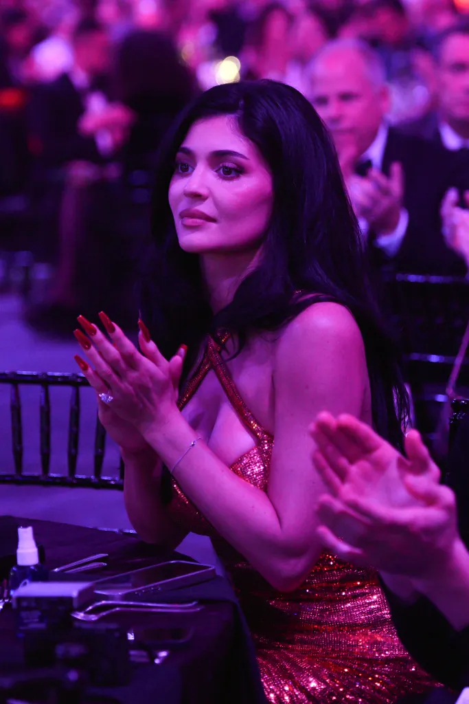 Kylie Jenner in a sparkly dress, clapping at an awards ceremony.