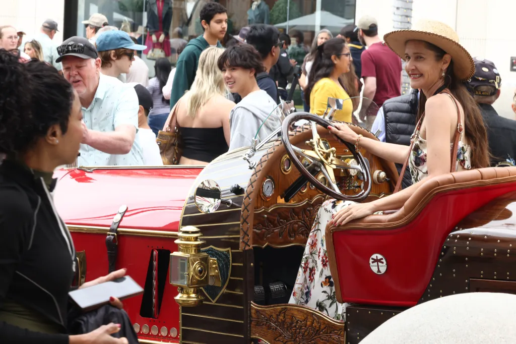 Kyra Steinbeck sitting in a red and wood vintage car at an outdoor event.