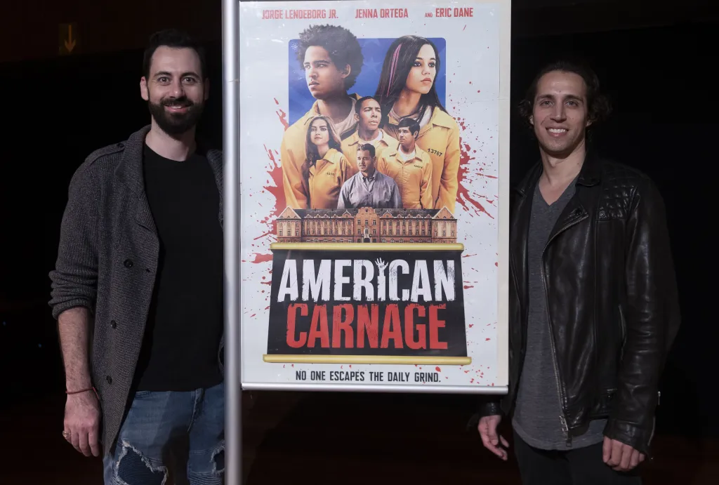 Diego Hallivis and Julio Hallivis next to a poster for their film 'American Carnage'.