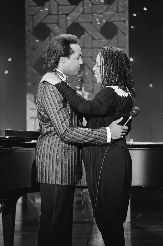 Black and white photo of Peabo Bryson and Roberta Flack embracing while holding microphones.