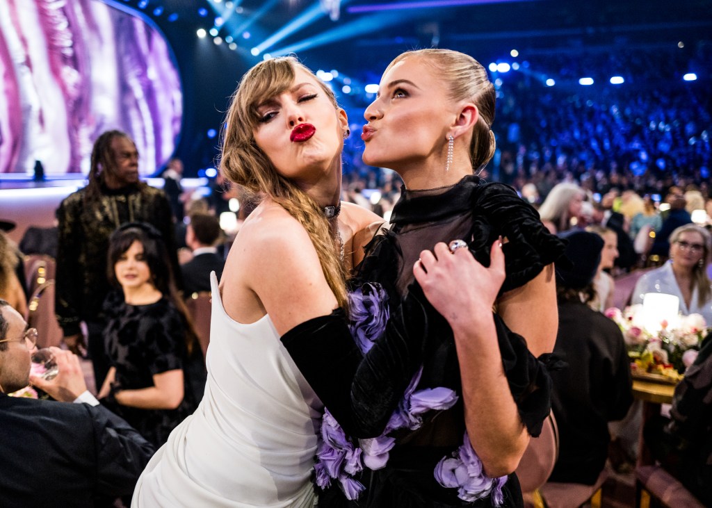 Taylor Swift in a white dress and Kelsea Ballerini in a black dress with purple flowers blowing kisses at the 66th GRAMMY Awards.